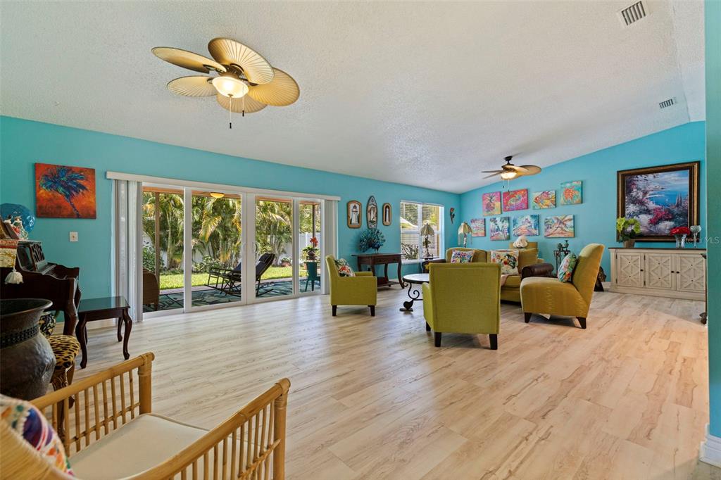 A bright living room features light wood-look flooring, turquoise walls, and large sliding glass doors — 201 58TH AVENUE S, ST PETERSBURG, FL