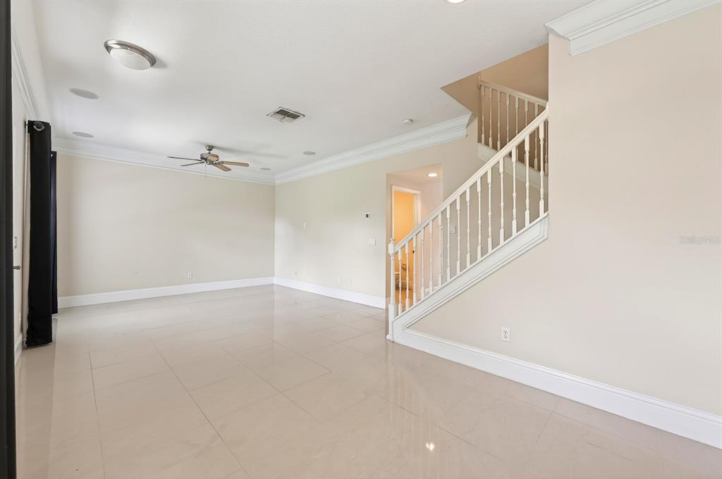 An empty living room features light-colored tile floors, a ceiling fan, and a wooden staircase — 6390 SOUTHBRIDGE STREET, WINDERMERE, FL