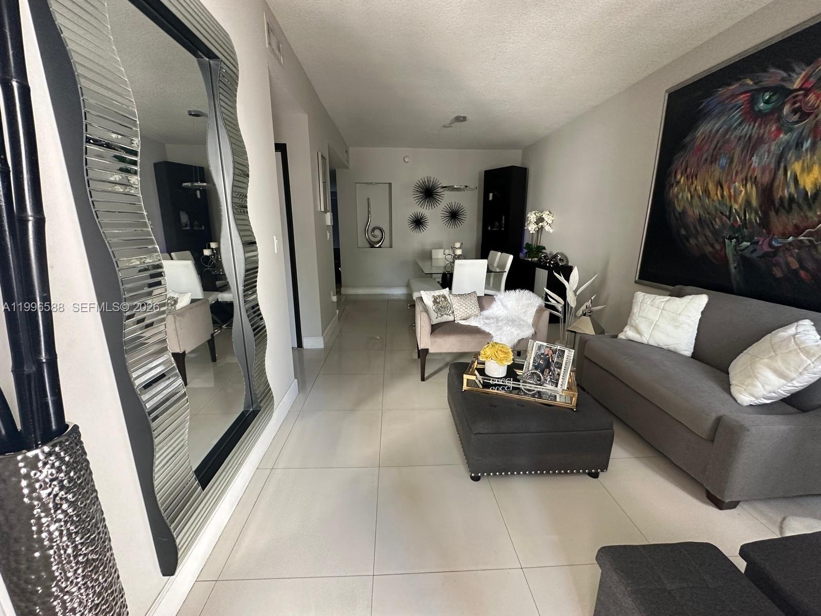 A living room features a large wavy mirror, gray sofa, ottoman, and dining area — 8441 SW 124th Ave # 106, Miami FL 33183, MIAMI, FL