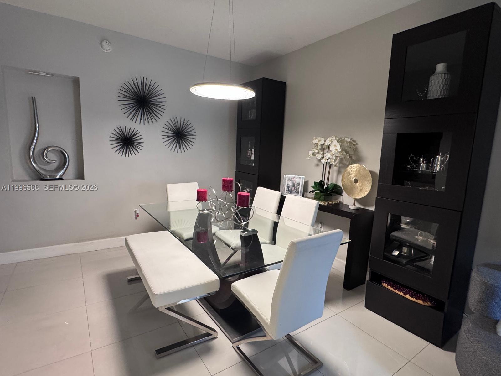A dining room features a glass table, white chairs, a bench, and dark cabinets — 8441 SW 124th Ave # 106, Miami FL 33183, MIAMI, FL