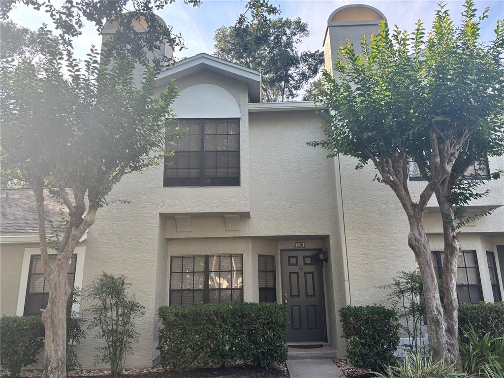 A two-story townhouse exterior with a gray front door, arched window, and landscaped front yard — 5100 BURCHETTE ROAD UNIT 1201, TAMPA, FL
