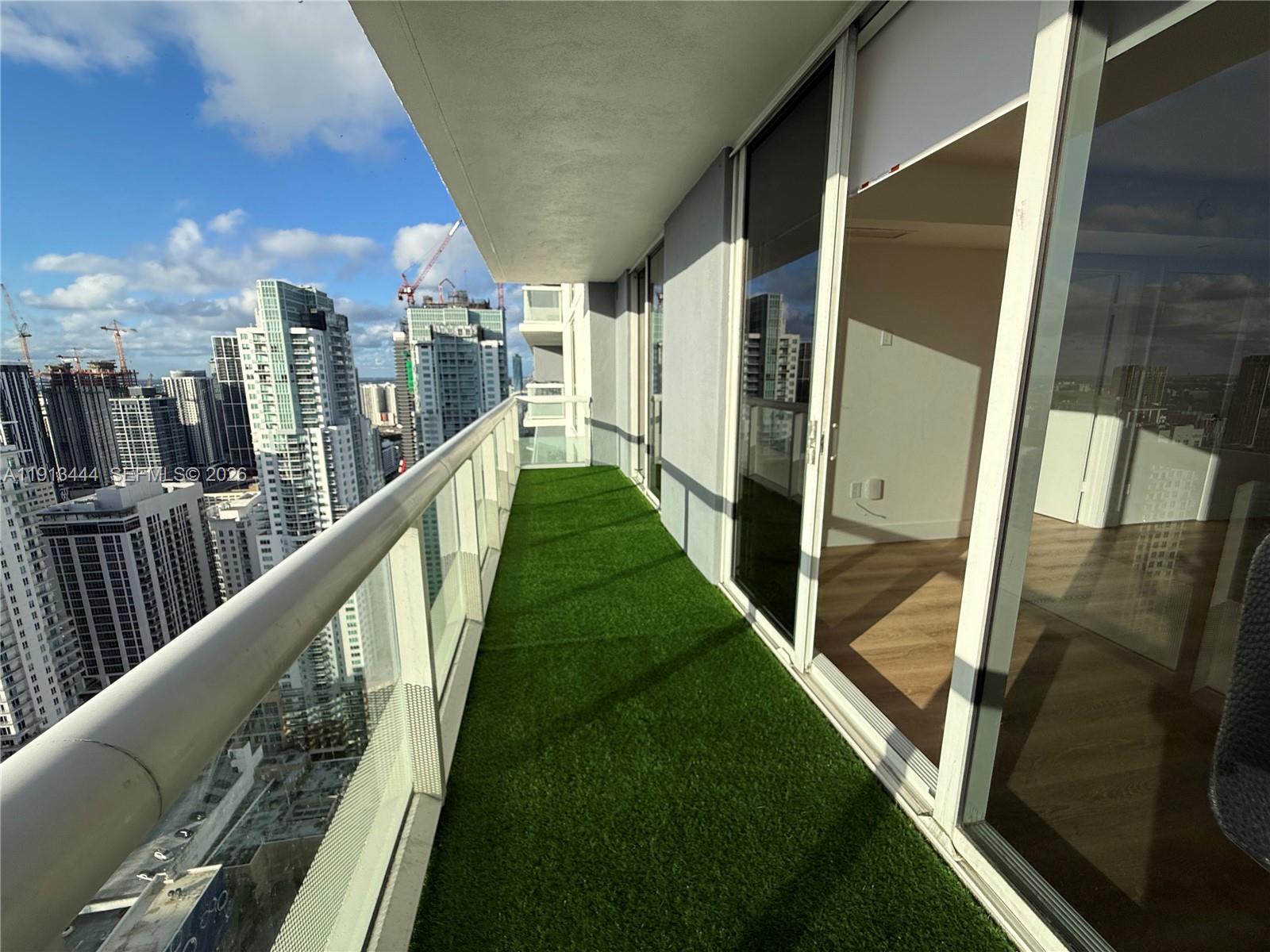 A high-rise balcony features artificial turf flooring and a glass railing overlooking a city skyline — 50 Biscayne Blvd # 4807, Miami FL 33132, MIAMI, FL