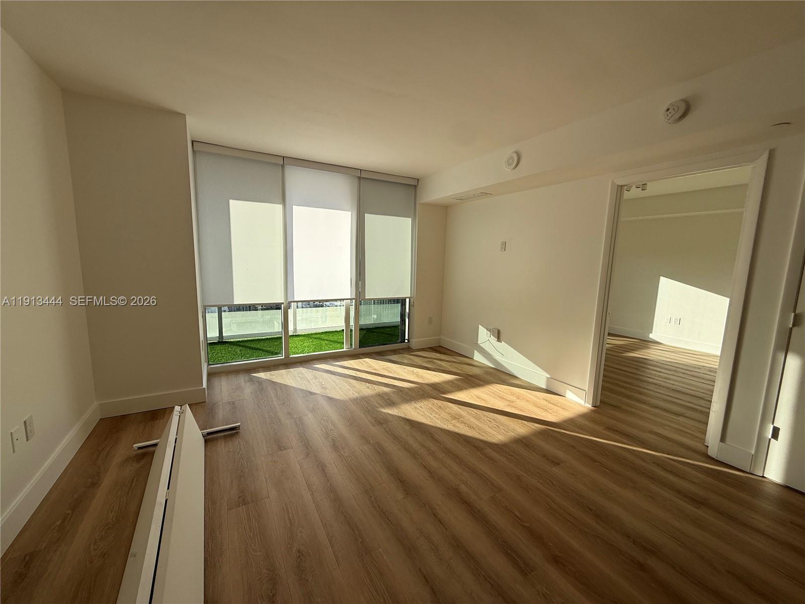 An empty room features light wood-look flooring, white walls, and a balcony with artificial turf — 50 Biscayne Blvd # 4807, Miami FL 33132, MIAMI, FL