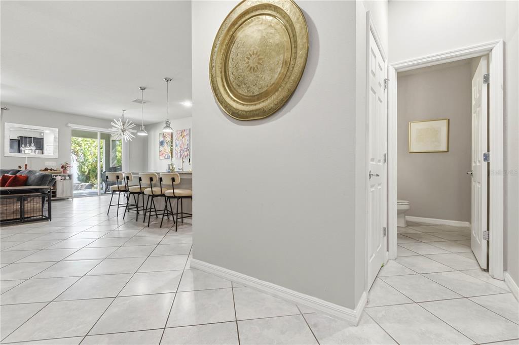 A tiled hallway leads to an open-concept kitchen and a bathroom with a white door — 11624 KILKENNY CORAL DRIVE, RIVERVIEW, FL