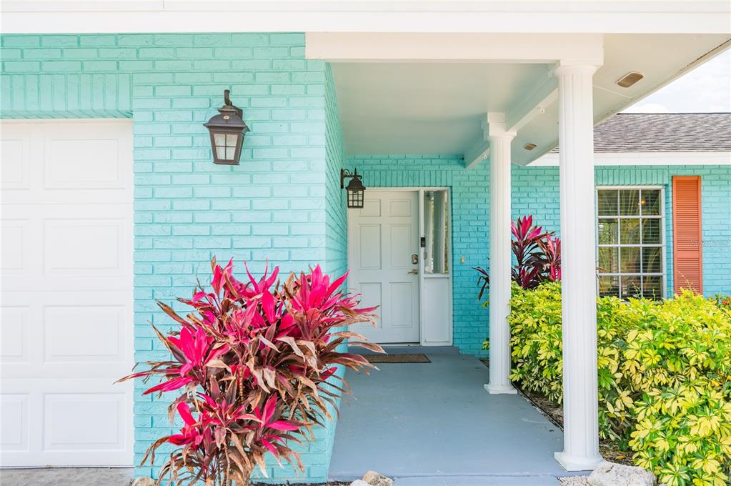 A turquoise brick house exterior features a white front door, columns, and vibrant landscaping — 1133 MONTEZUMA DRIVE, BRADENTON, FL