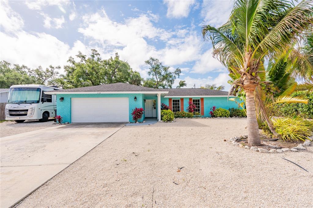 A single-story turquoise brick house with a white garage door and a gravel driveway — 1133 MONTEZUMA DRIVE, BRADENTON, FL