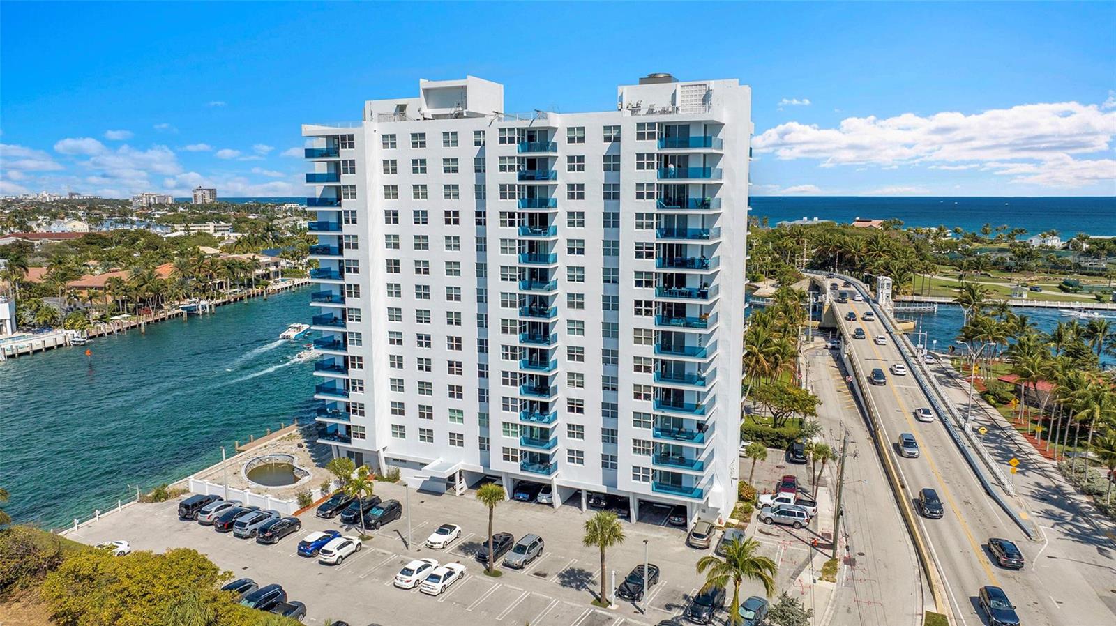 An aerial view shows a white high-rise apartment building situated between a waterway and road — 2639 N Riverside Drive # 1005, Pompano Beach FL 33062, POMPANO BEACH, FL