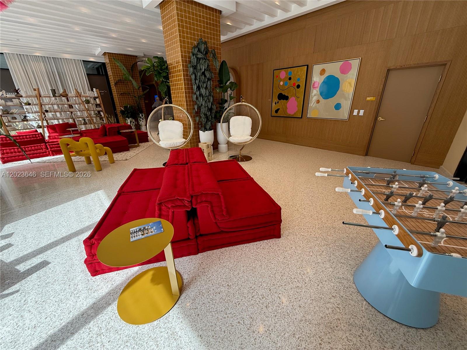 A modern lounge area features red modular seating, hanging chairs, and a blue foosball table — 90 NE 32 # 411, Miami FL 33137, MIAMI, FL