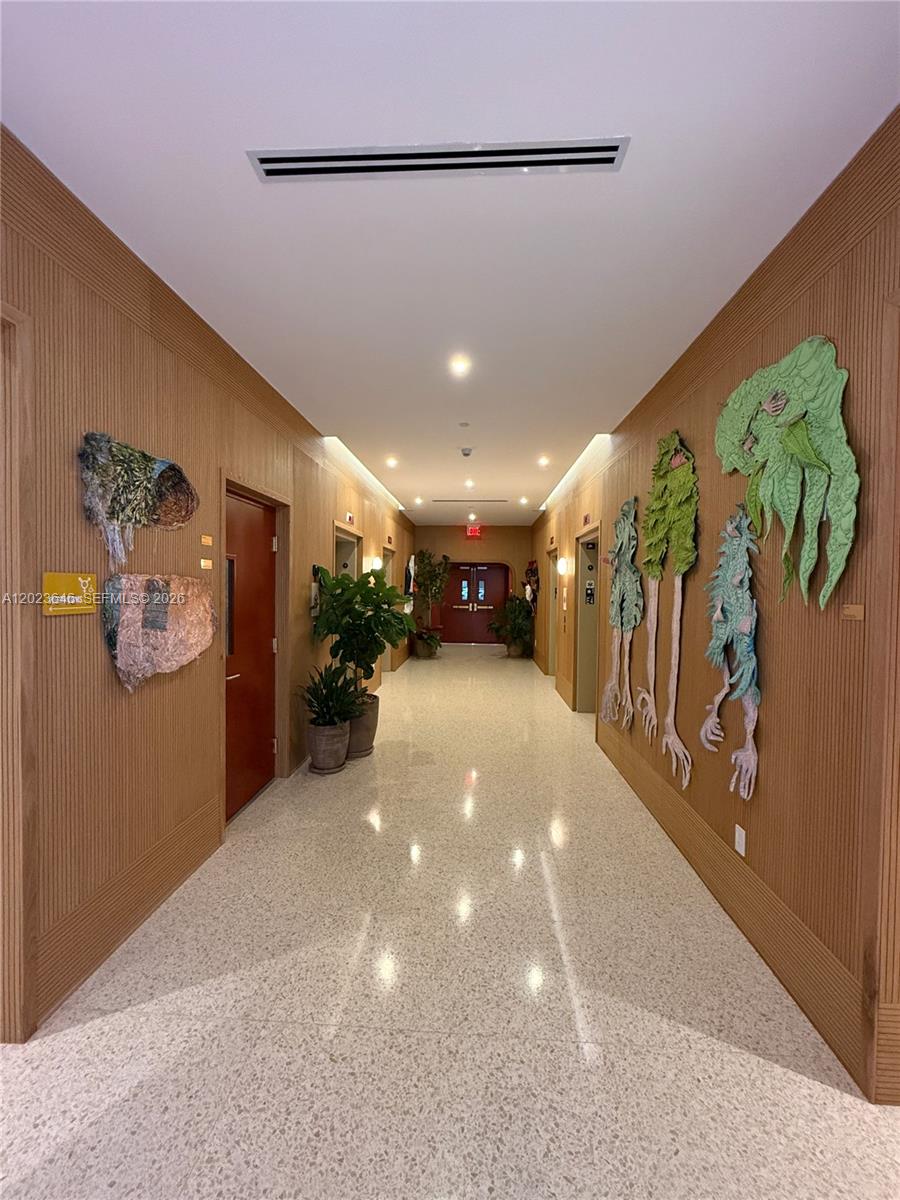 A hallway features wood-paneled walls, textured wall art, potted plants, and a light-colored terrazzo floor — 90 NE 32 # 411, Miami FL 33137, MIAMI, FL