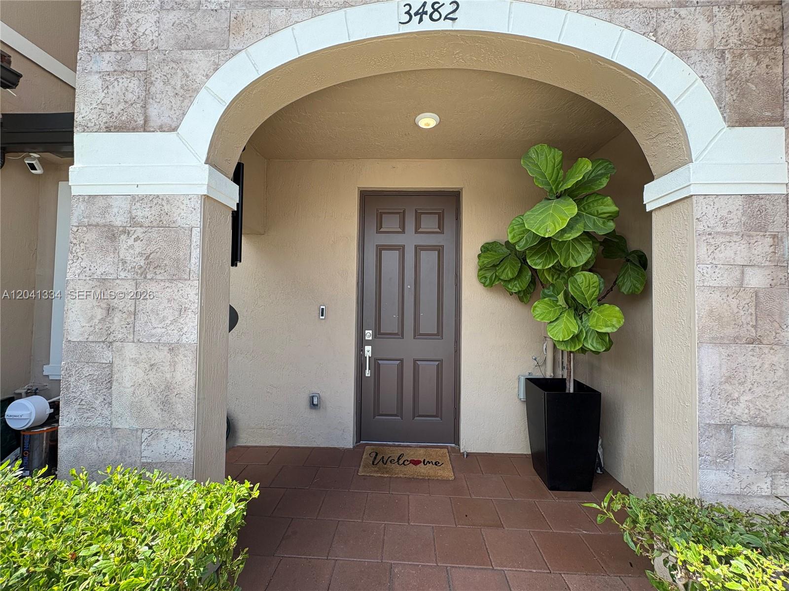 A brown front door sits under a stone archway with a large potted plant nearby — 3482 W 114th Ter, Hialeah FL 33018, HIALEAH, FL