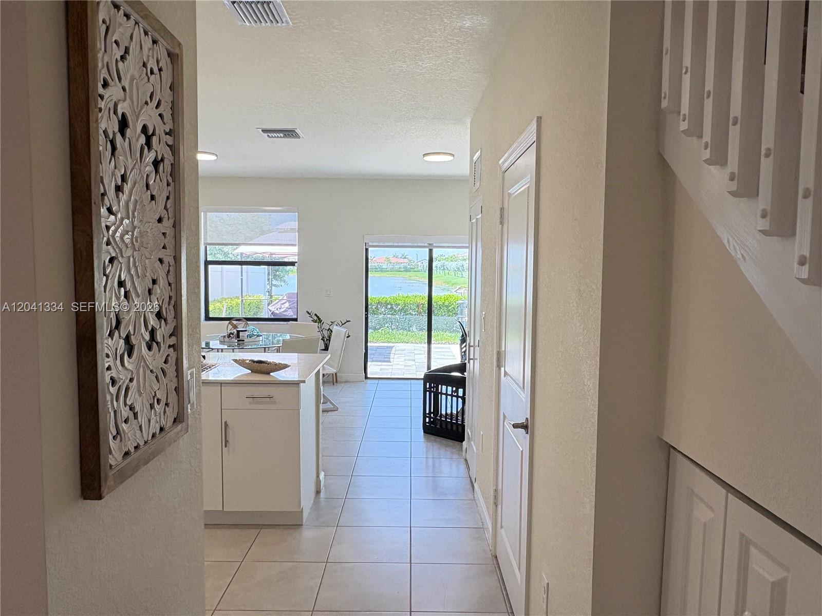 A hallway leads past a kitchen island toward a sliding glass door overlooking a lake — 3482 W 114th Ter, Hialeah FL 33018, HIALEAH, FL