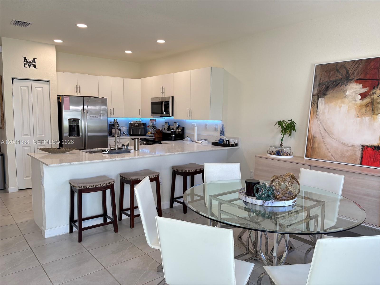 A kitchen with white cabinets and a breakfast bar overlooks a glass dining table — 3482 W 114th Ter, Hialeah FL 33018, HIALEAH, FL