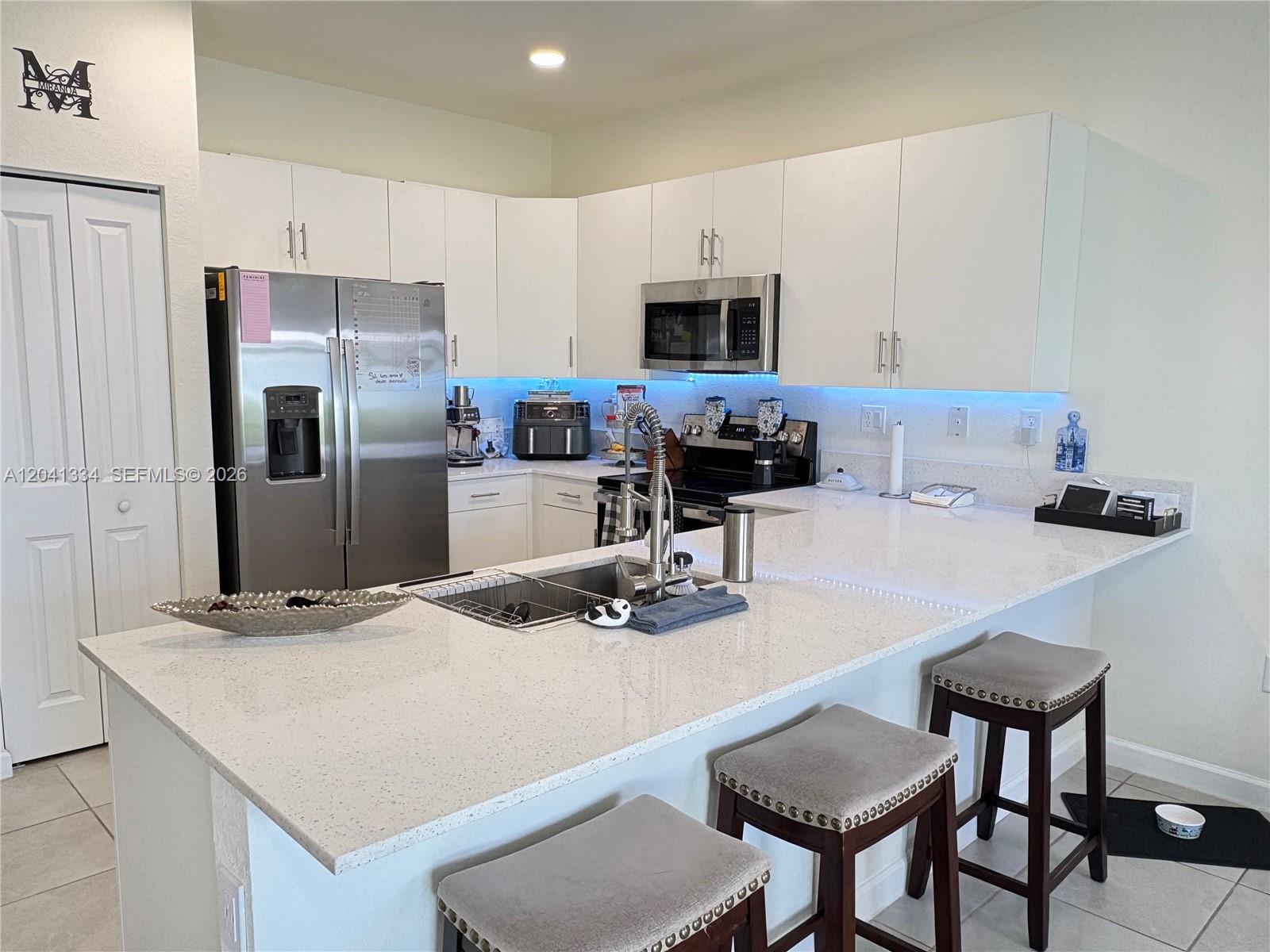 A modern kitchen features white cabinets, stainless steel appliances, and a large quartz-topped island — 3482 W 114th Ter, Hialeah FL 33018, HIALEAH, FL