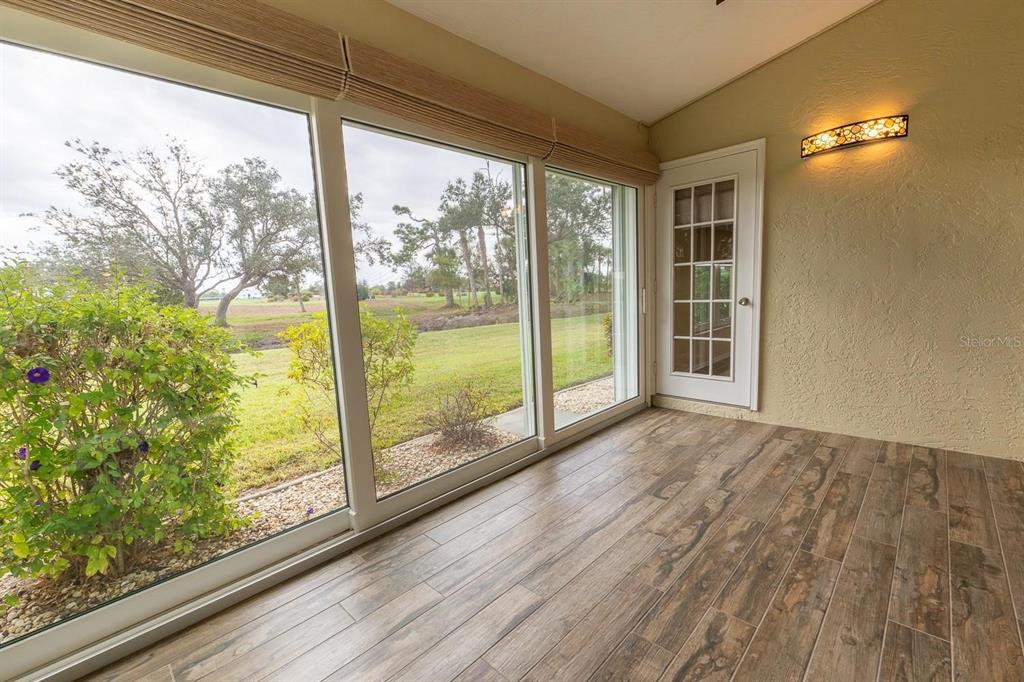 A sunroom features wood-look tile flooring, large windows overlooking a golf course, and a door — 12235 SW KINGSWAY CIRCLE UNIT C6, ARCADIA, FL