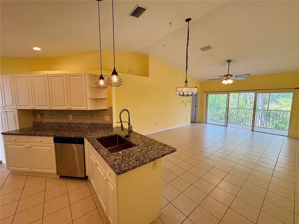 A kitchen with white cabinets and granite countertops opens into a tiled living area — 6421 BAY CEDAR LANE, BRADENTON, FL