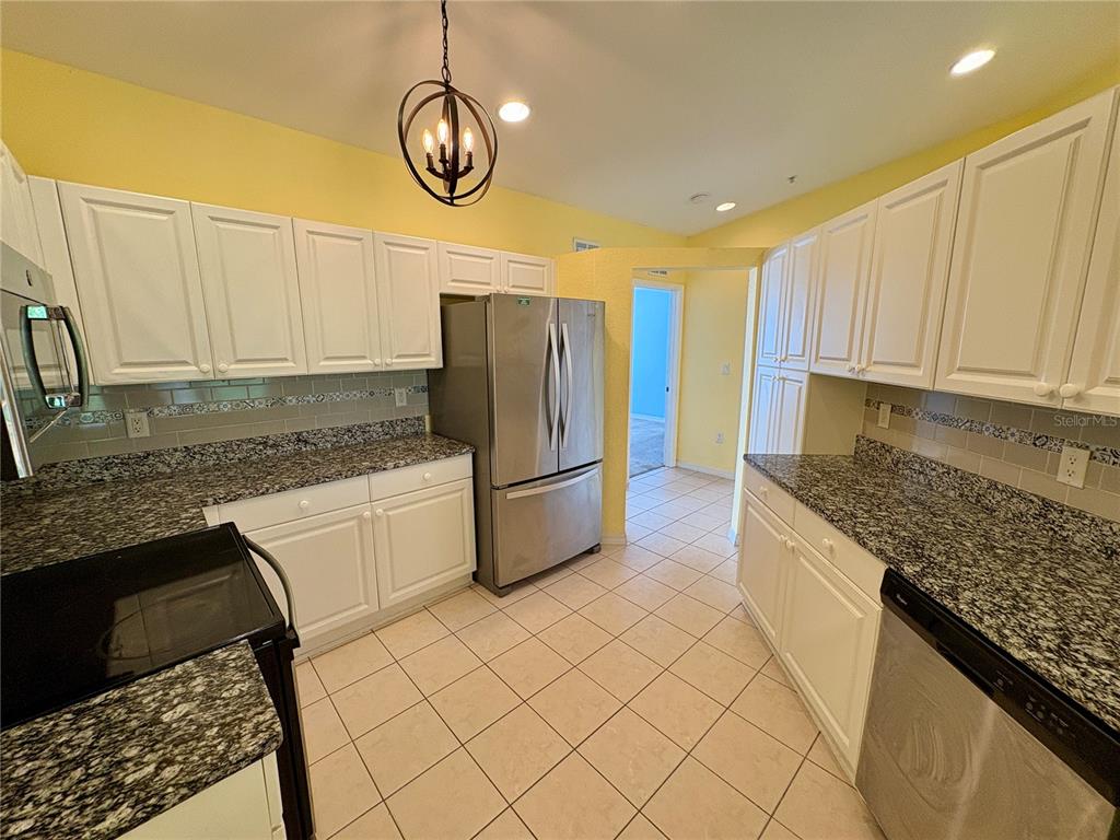 A kitchen features white cabinets, granite countertops, stainless steel appliances, and light-colored tile flooring — 6421 BAY CEDAR LANE, BRADENTON, FL