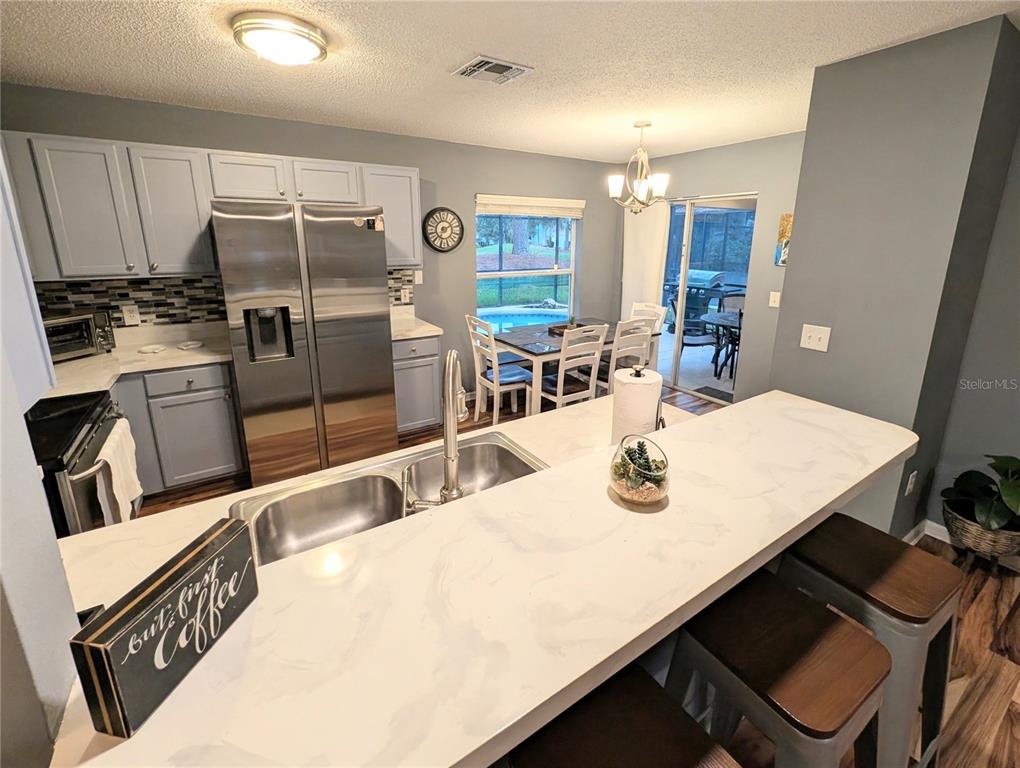A living room with wood-look flooring, a gray sectional sofa, and an open kitchen area — 2976 KOKOMO LOOP, HAINES CITY, FL