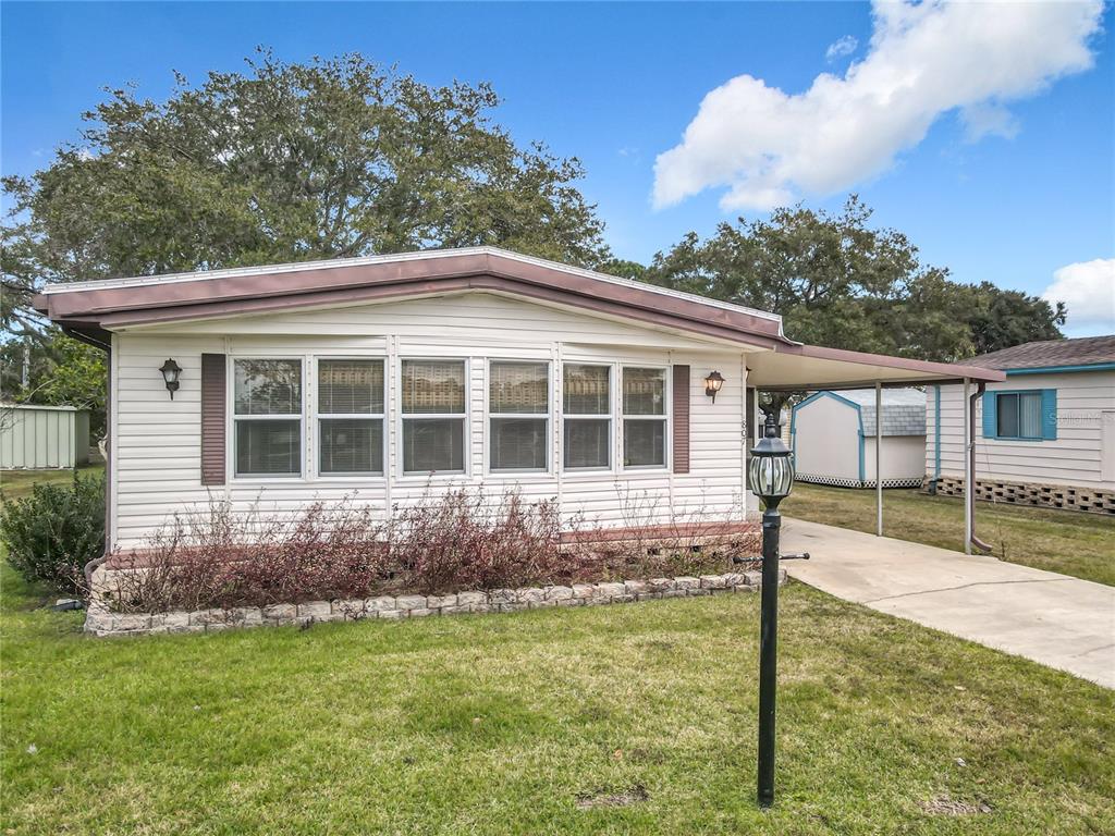 A single-story manufactured home with white siding, a front carport, and a stone garden border — 807 SWALLOW LANE, OSTEEN, FL
