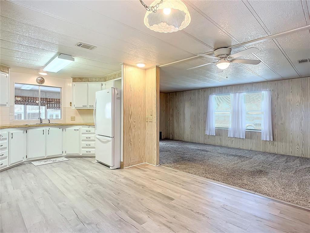A kitchen with white cabinets and wood-look flooring opens into a carpeted living area — 807 SWALLOW LANE, OSTEEN, FL