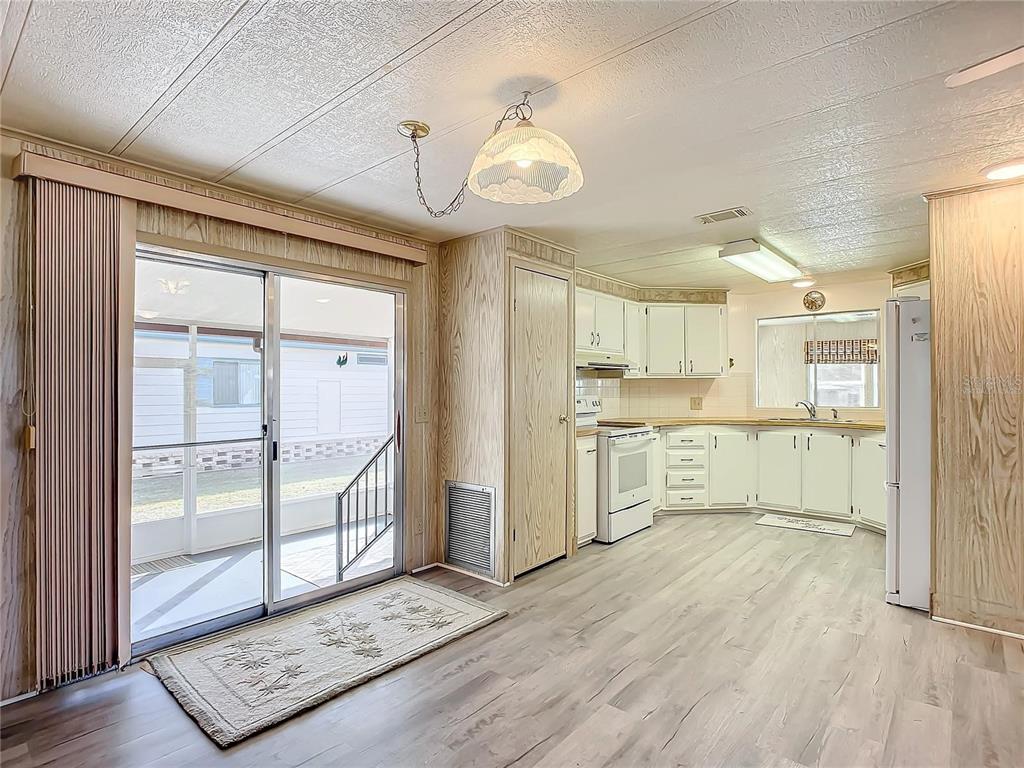 A kitchen and dining area with wood-paneled walls, white cabinets, and sliding glass patio doors — 807 SWALLOW LANE, OSTEEN, FL