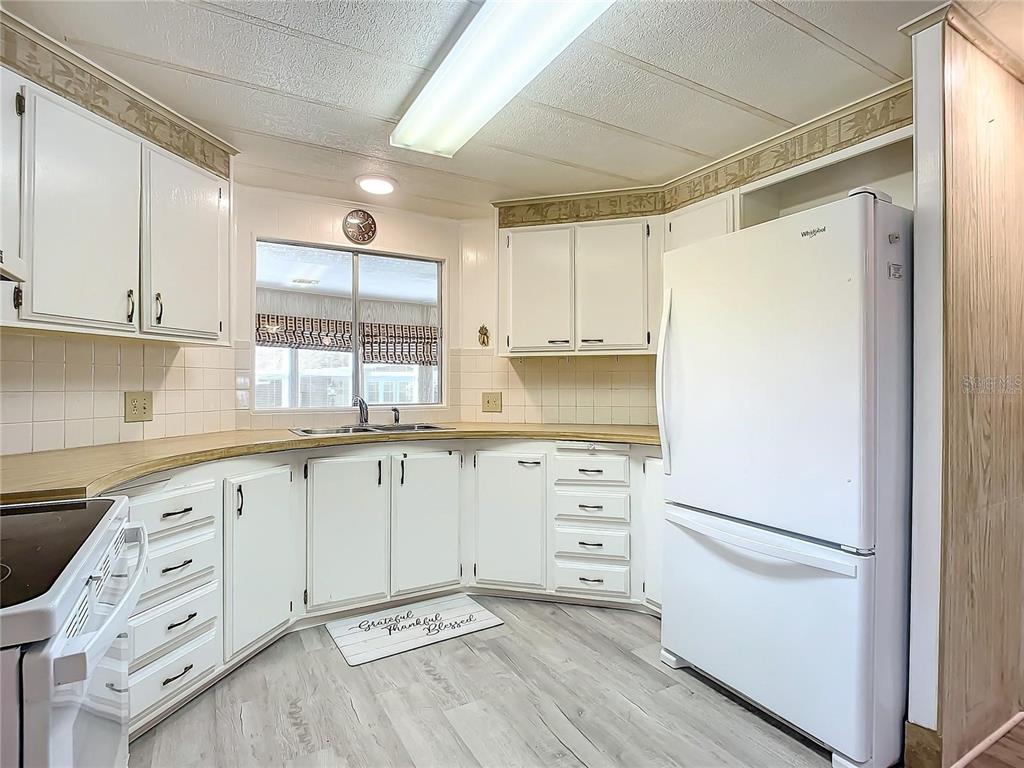 A kitchen features white cabinets, a light wood countertop, a white refrigerator, and light flooring — 807 SWALLOW LANE, OSTEEN, FL
