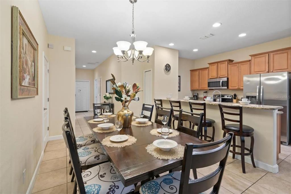 A dining area with a long wooden table and chairs sits adjacent to a kitchen — 3071 BEACH PALM AVENUE, KISSIMMEE, FL