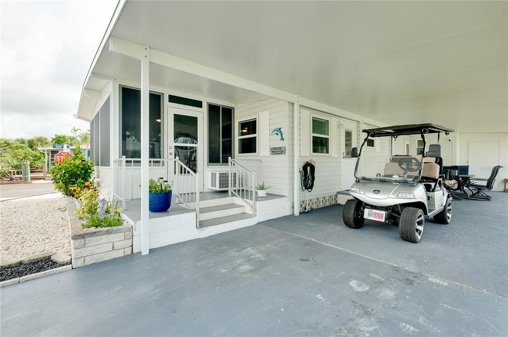 A mobile home exterior features a covered carport, a golf cart, and a small porch — 214 ROMA ROAD, VENICE, FL