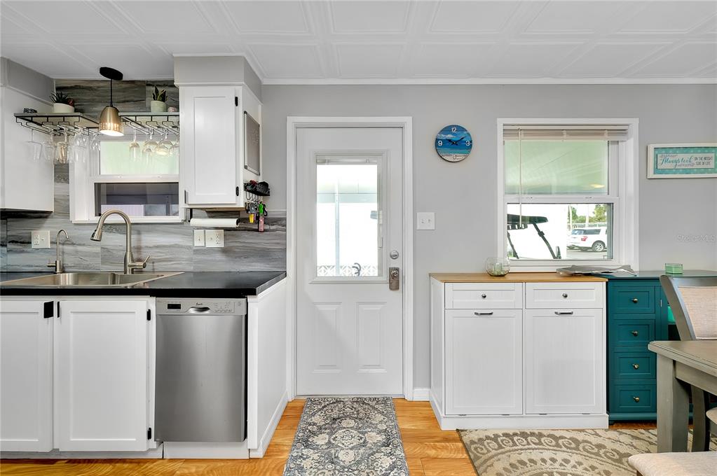 A kitchen with white cabinets, a stainless steel dishwasher, wood flooring, and a glass-paneled door — 214 ROMA ROAD, VENICE, FL