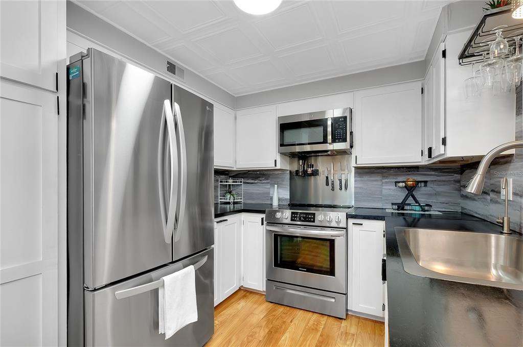 A kitchen features stainless steel appliances, white cabinets, dark countertops, and a gray tiled backsplash — 214 ROMA ROAD, VENICE, FL