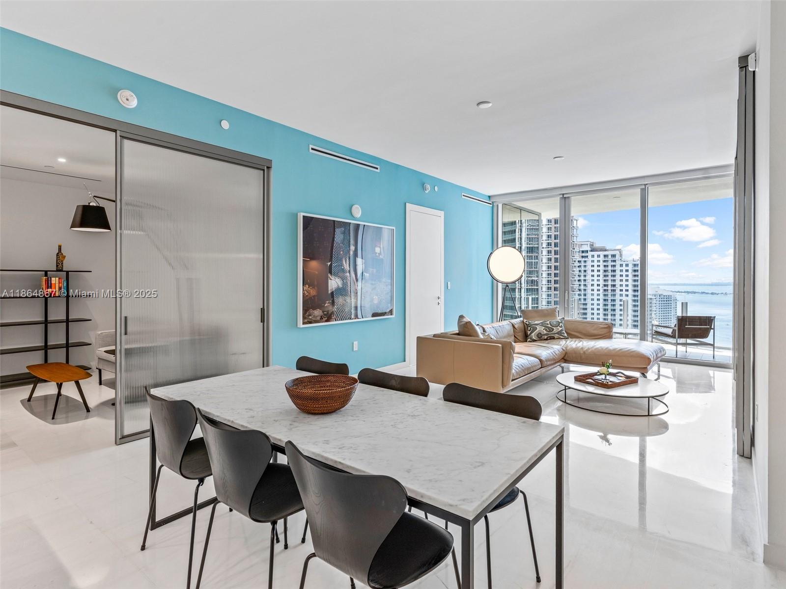 A modern living and dining area features a light blue wall, marble floors, and balcony views — 300 Biscayne Blvd Way # 2505, Miami FL 33131, MIAMI, FL