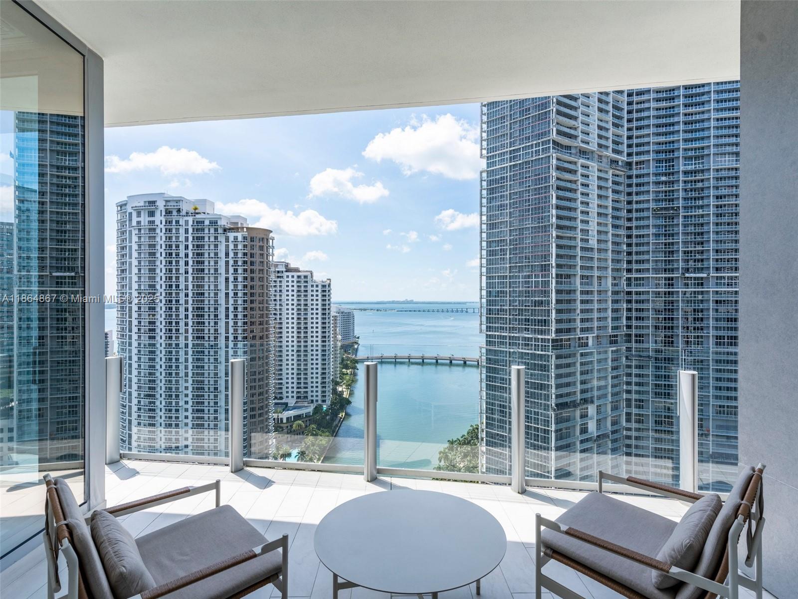 A balcony with two chairs and a table overlooks a bay and city skyscrapers — 300 Biscayne Blvd Way # 2505, Miami FL 33131, MIAMI, FL
