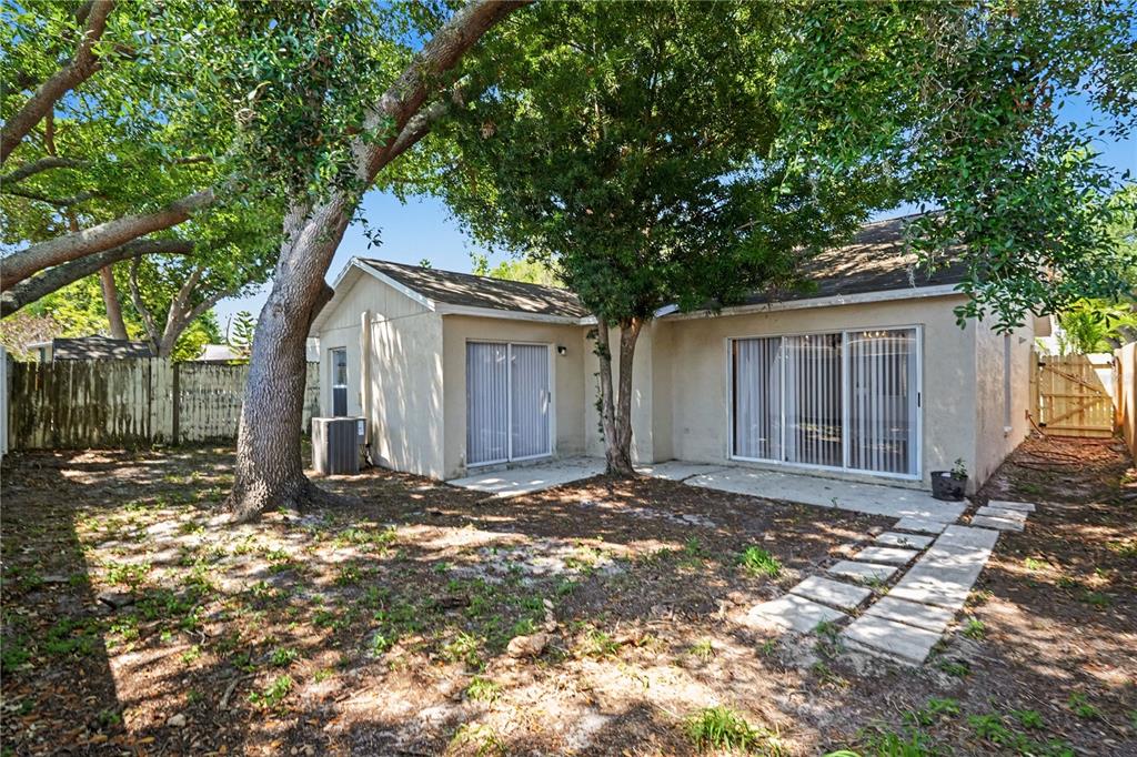 The backyard of a house features a concrete patio, sliding glass doors, and large trees — 13618 LARAWAY DRIVE, RIVERVIEW, FL
