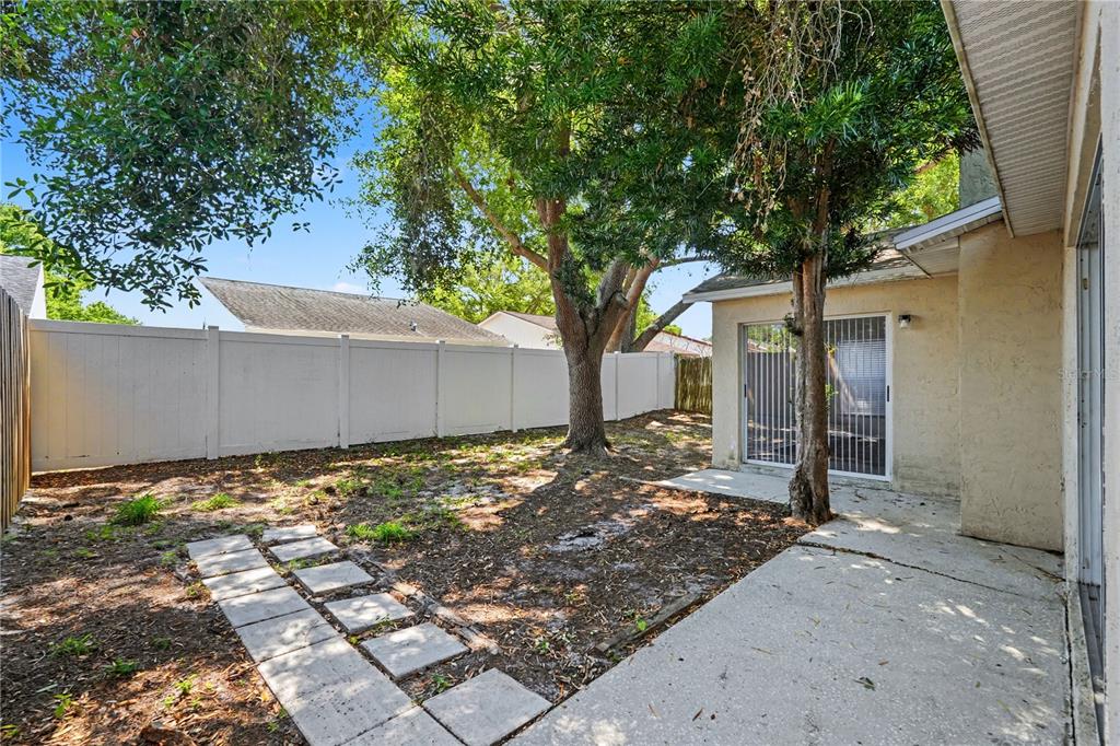 A backyard with a concrete patio, a large tree, and a white vinyl privacy fence — 13618 LARAWAY DRIVE, RIVERVIEW, FL