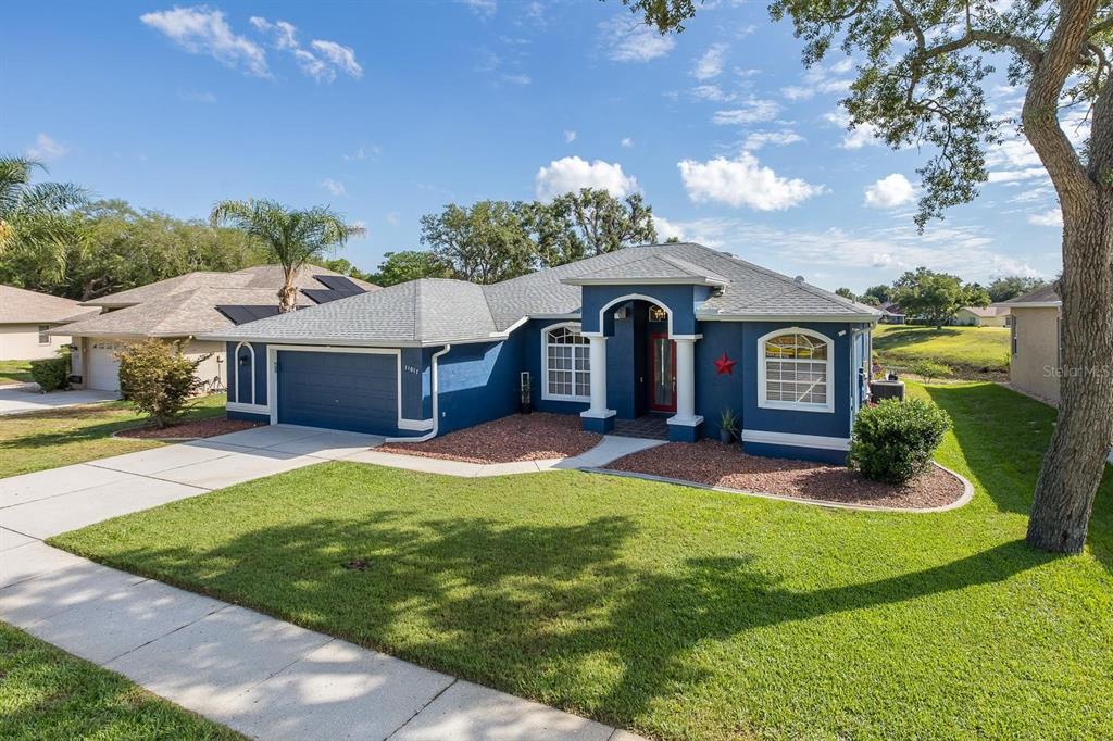 A blue single-story house with a two-car garage and a front walkway on a lawn — 11017 AUDIE BROOK DRIVE, SPRING HILL, FL