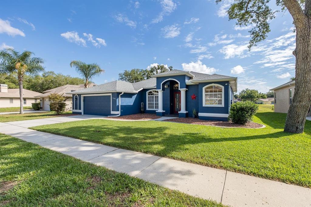 A blue single-story house with a two-car garage, arched entryway, and a large front lawn — 11017 AUDIE BROOK DRIVE, SPRING HILL, FL