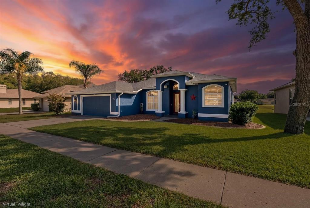 A blue single-story house with a two-car garage sits under a vibrant sunset sky — 11017 AUDIE BROOK DRIVE, SPRING HILL, FL