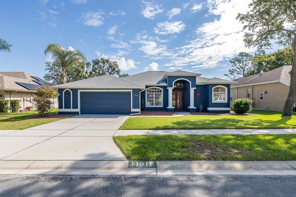A blue single-story house with a two-car garage and a red front door — 11017 AUDIE BROOK DRIVE, SPRING HILL, FL