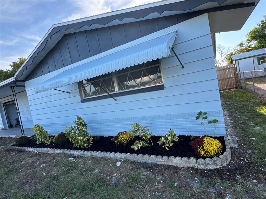 A light blue house exterior features a metal window awning and a landscaped flower bed — 3447 COLUMBUS DRIVE, HOLIDAY, FL