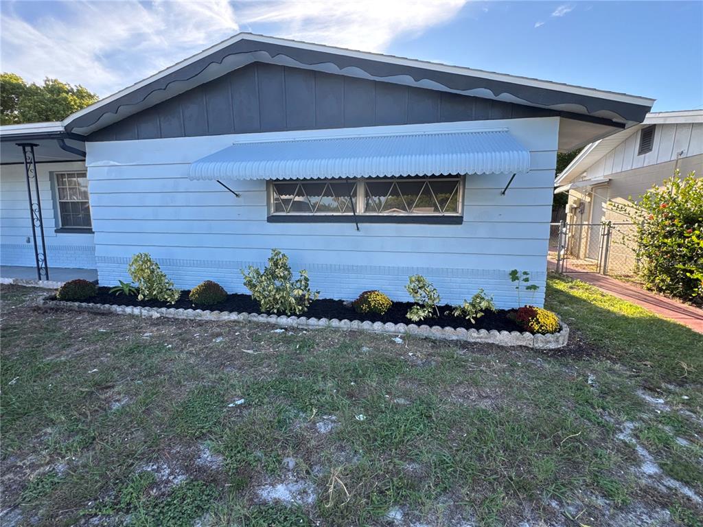 The exterior of a light blue house features a metal awning over a horizontal window — 3447 COLUMBUS DRIVE, HOLIDAY, FL
