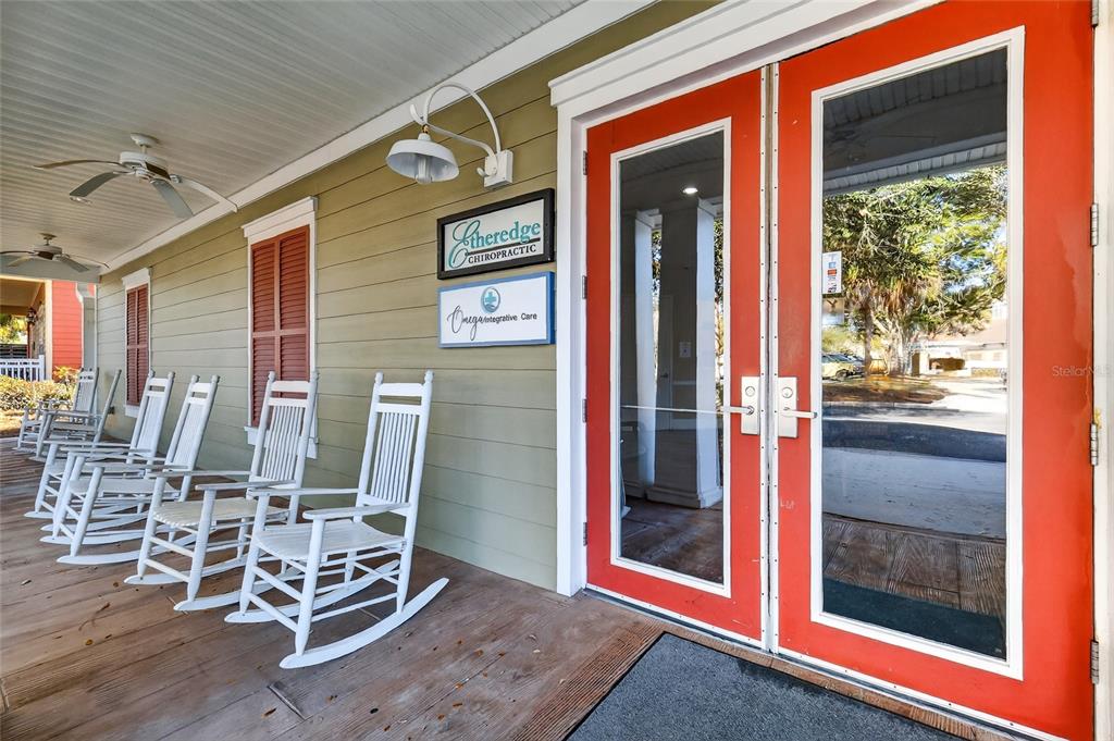 A covered porch features white rocking chairs, a red double door, and professional signage — 910 OLD CAMP ROAD UNIT 110, THE VILLAGES, FL