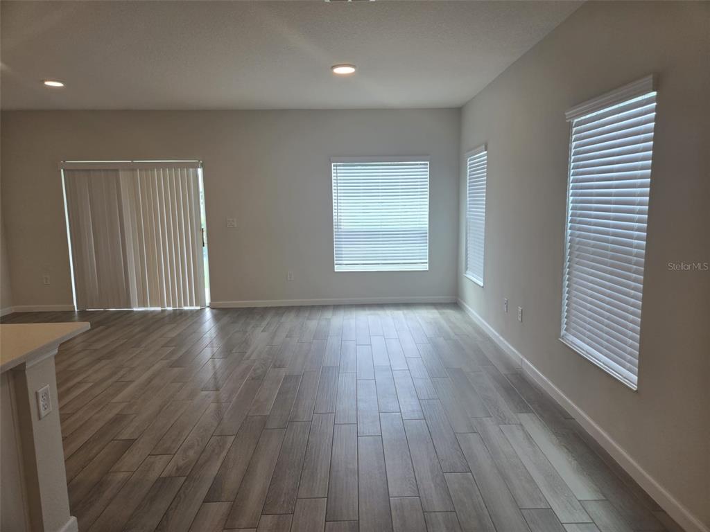 An empty living area features gray wood-look tile flooring, light walls, and multiple windows — 2802 NARCOOSSEE COMMONS WAY, ST CLOUD, FL