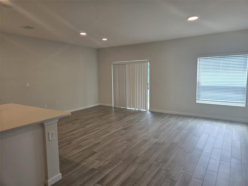 An empty living room features light-colored walls, wood-look tile flooring, a sliding glass door, and windows — 2802 NARCOOSSEE COMMONS WAY, ST CLOUD, FL
