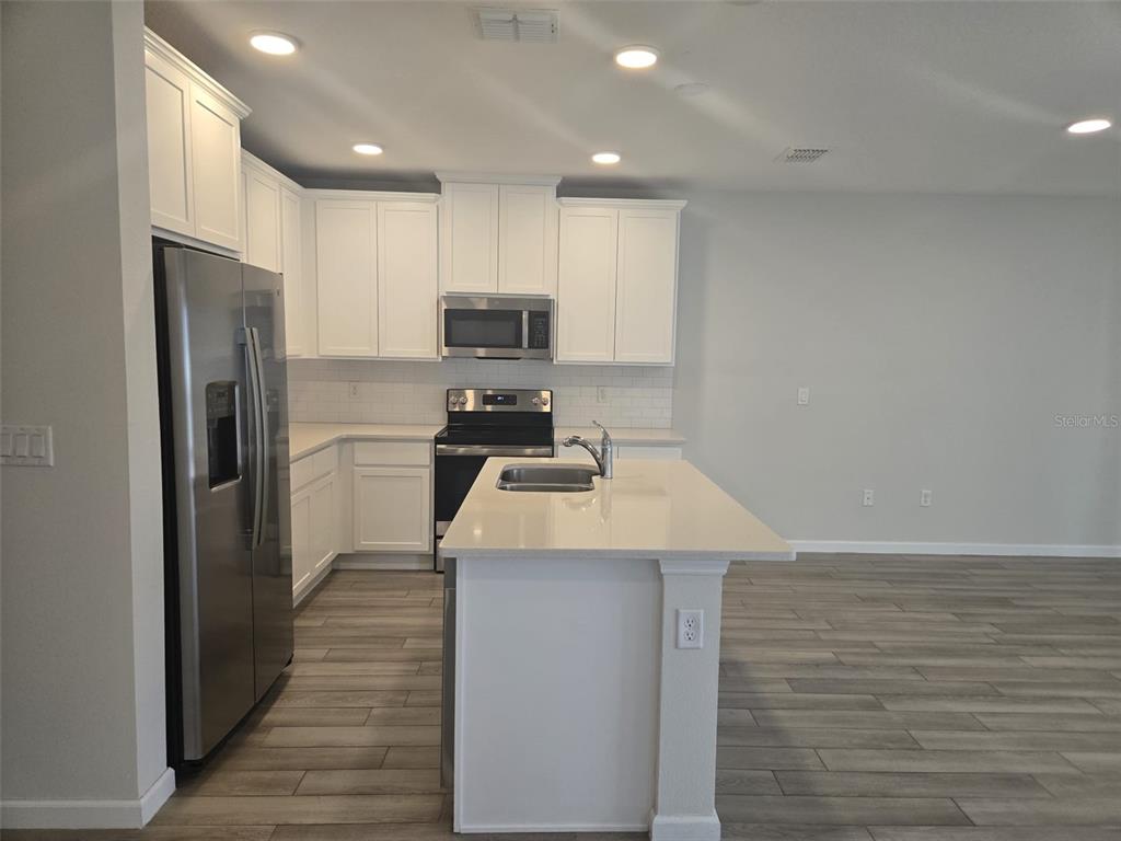 A modern kitchen features white cabinets, stainless steel appliances, a center island, and wood-look flooring — 2802 NARCOOSSEE COMMONS WAY, ST CLOUD, FL