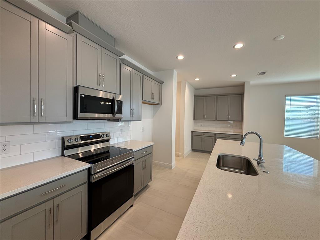 A modern kitchen features gray cabinets, white countertops, stainless steel appliances, and a central island — 1867 CHURCH LAKE STREET, GROVELAND, FL