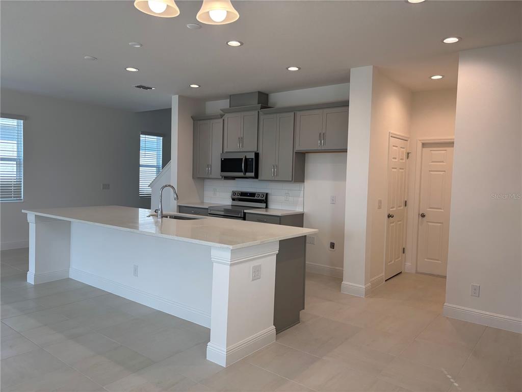 A modern kitchen features a large white island, gray cabinetry, and light-colored tile flooring — 1867 CHURCH LAKE STREET, GROVELAND, FL