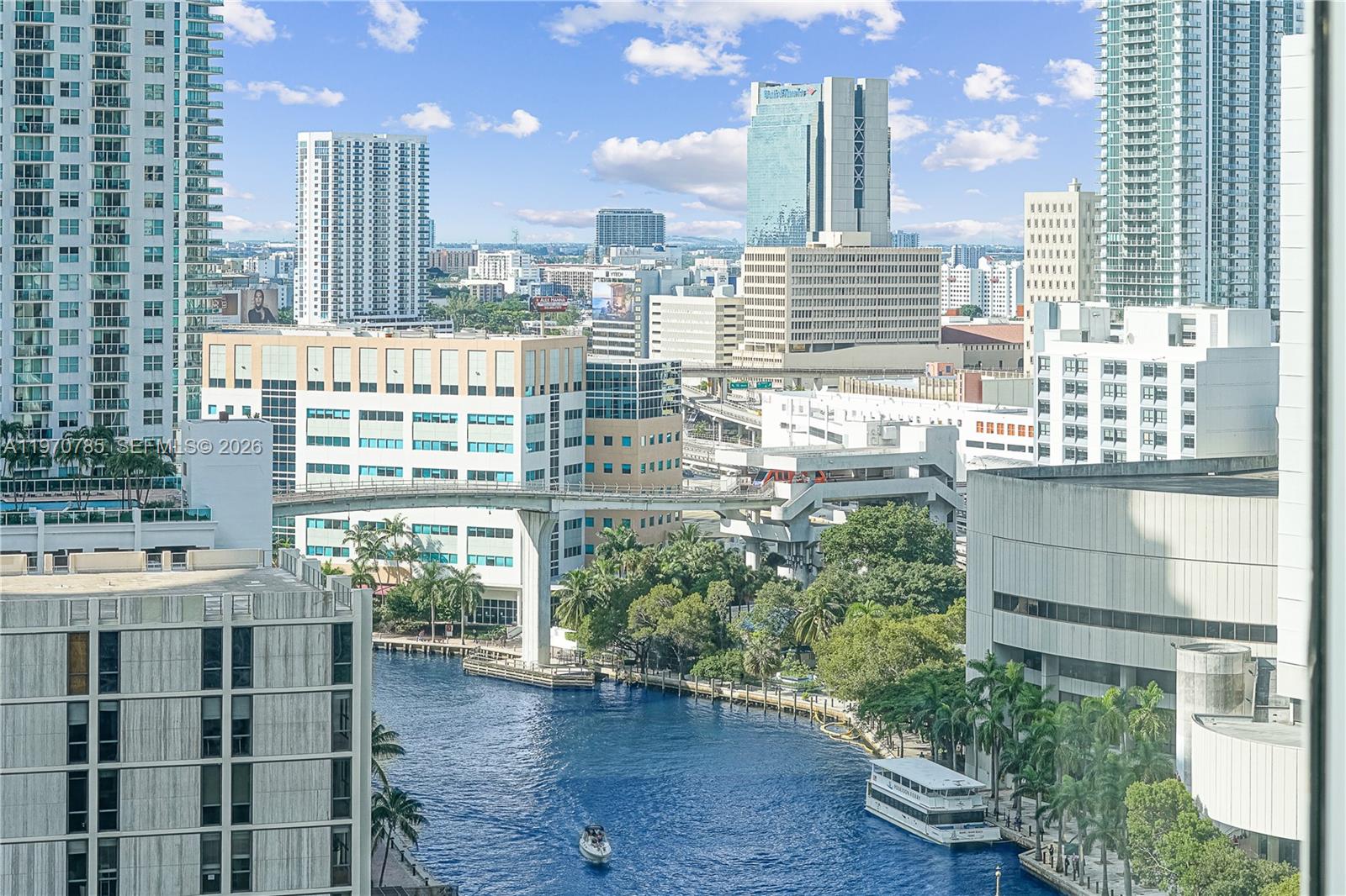 An elevated view of a city canal with a boat, surrounding buildings, and a monorail track — 475 Brickell Ave # 1913, Miami FL 33131, MIAMI, FL