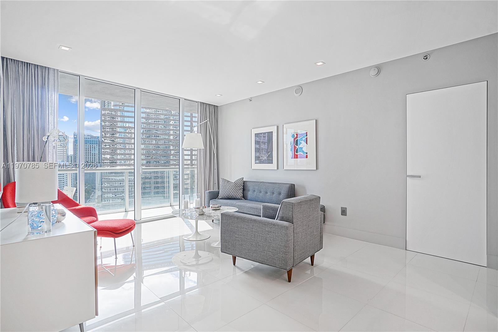 A modern living room features gray furniture, white tile floors, and floor-to-ceiling windows — 475 Brickell Ave # 1913, Miami FL 33131, MIAMI, FL