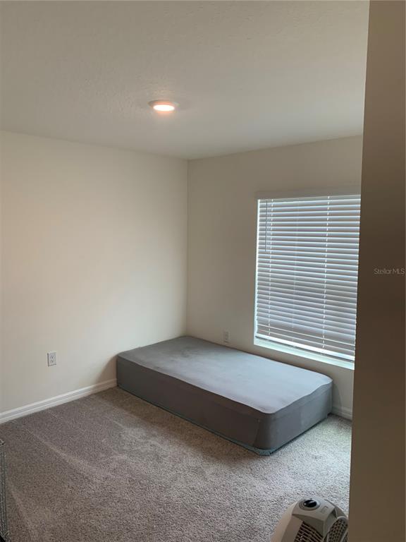 A bedroom with beige walls, gray carpet, a single window with blinds, and an air mattress — 10305 SE 161ST STREET, SUMMERFIELD, FL