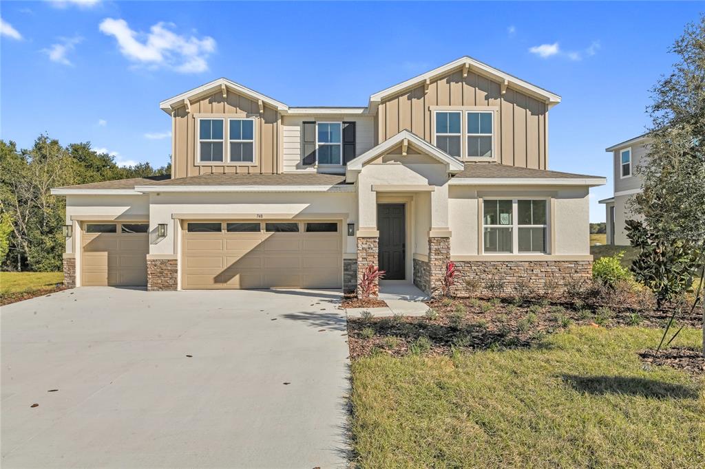 A two-story house with a three-car garage, stone accents, and tan siding under a blue sky — 748 WEKIVA RIDGE DRIVE, MOUNT DORA, FL