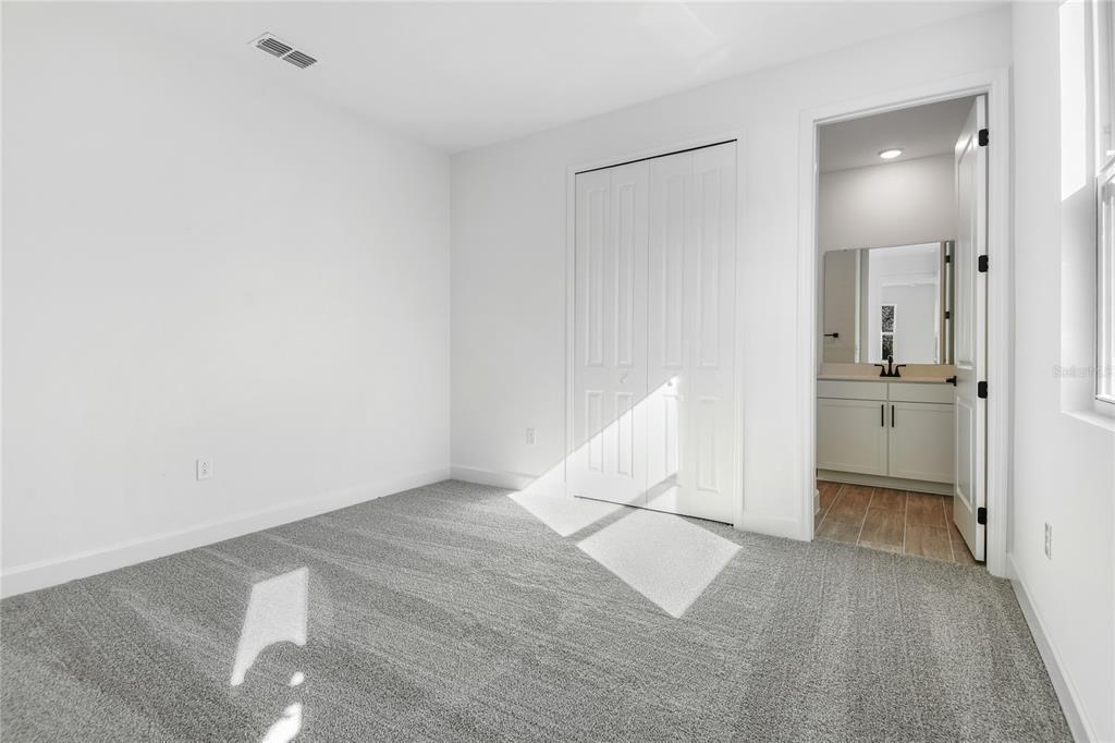 An empty bedroom with gray carpet, white walls, a closet, and an attached bathroom — 748 WEKIVA RIDGE DRIVE, MOUNT DORA, FL